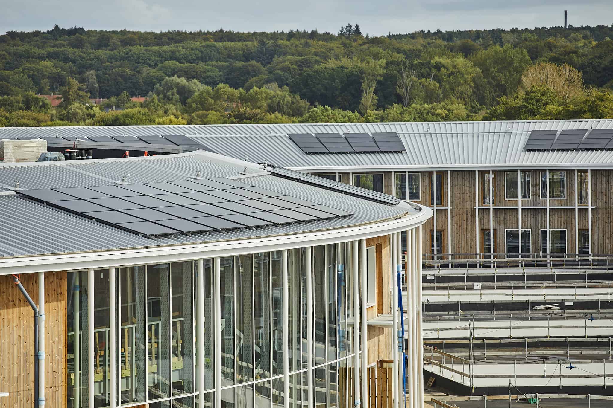 Moderne træbygning monteret med solceller til erhverv på buet metaltag fra Solar Polaris.